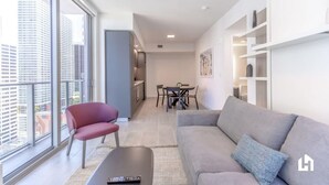 A modern living room with a grey sofa, a red chair, and a dining area with a table and chairs. - Downtown Condo with City Views, Pool, Near Bayside (Miami)