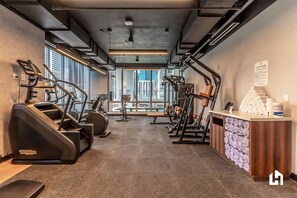 A gym with treadmills, elliptical machines, and weight equipment, with a reception desk and a view of the city.