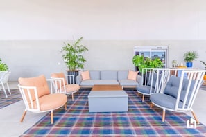 A modern lounge area with a grey sofa, white armchairs, and a colorful plaid rug.