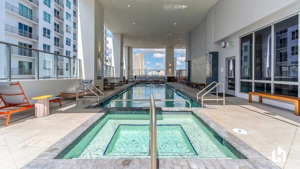 A modern indoor pool area with a clear view of the city skyline, featuring a long pool with a central divider, lounge chairs, and a seating area. - Bayside District Studio: City Views & Pool (Miami)