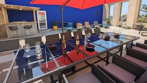 Eine Terrassenanlage im Freien mit einem Glastisch, Korbstühlen und einem roten Sonnenschirm.