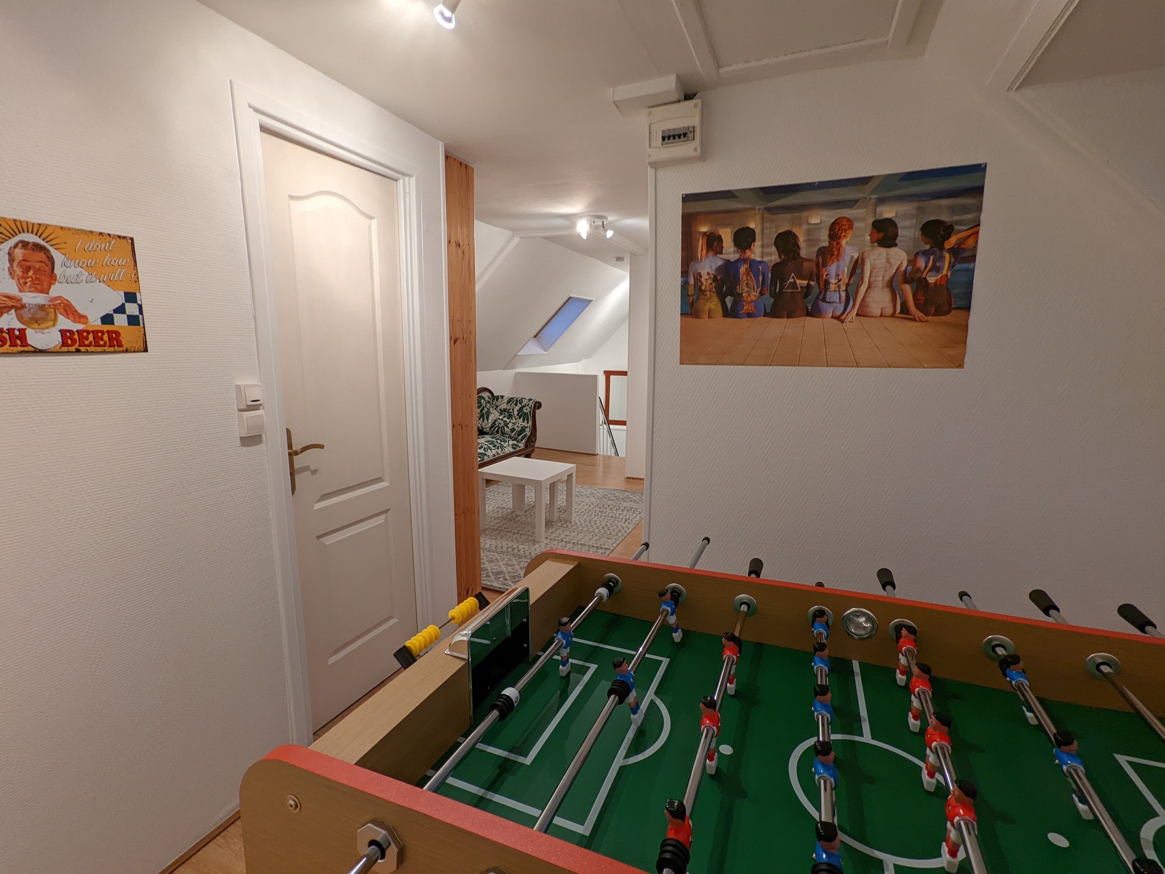 A room with a foosball table, a sofa, a painting, and a door.