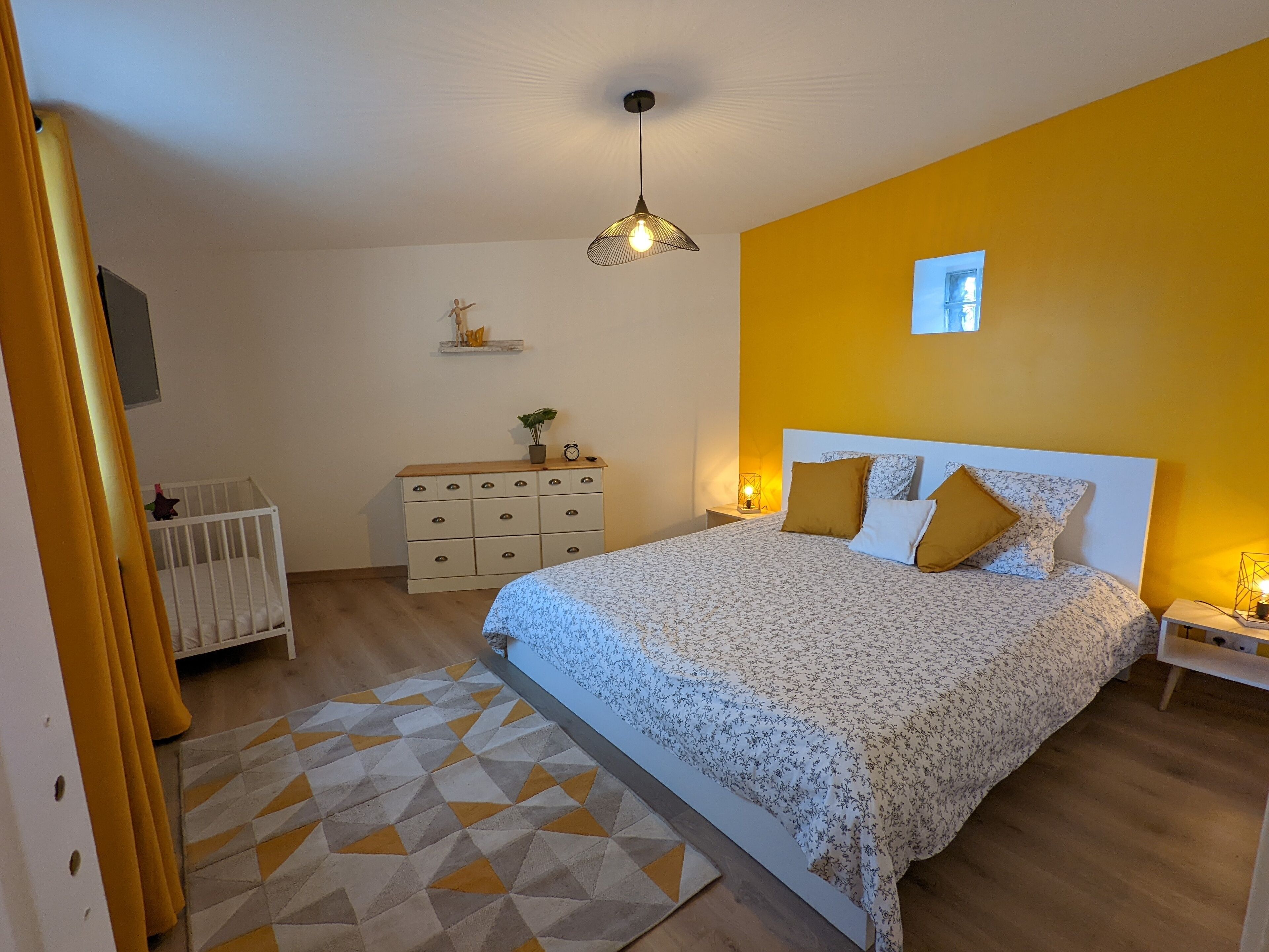 A bedroom with a bed, a dresser, a nightstand, a lamp, and a geometric rug.