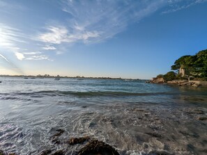 A coastal scene with clear water, boats, and a rocky shoreline with a building.