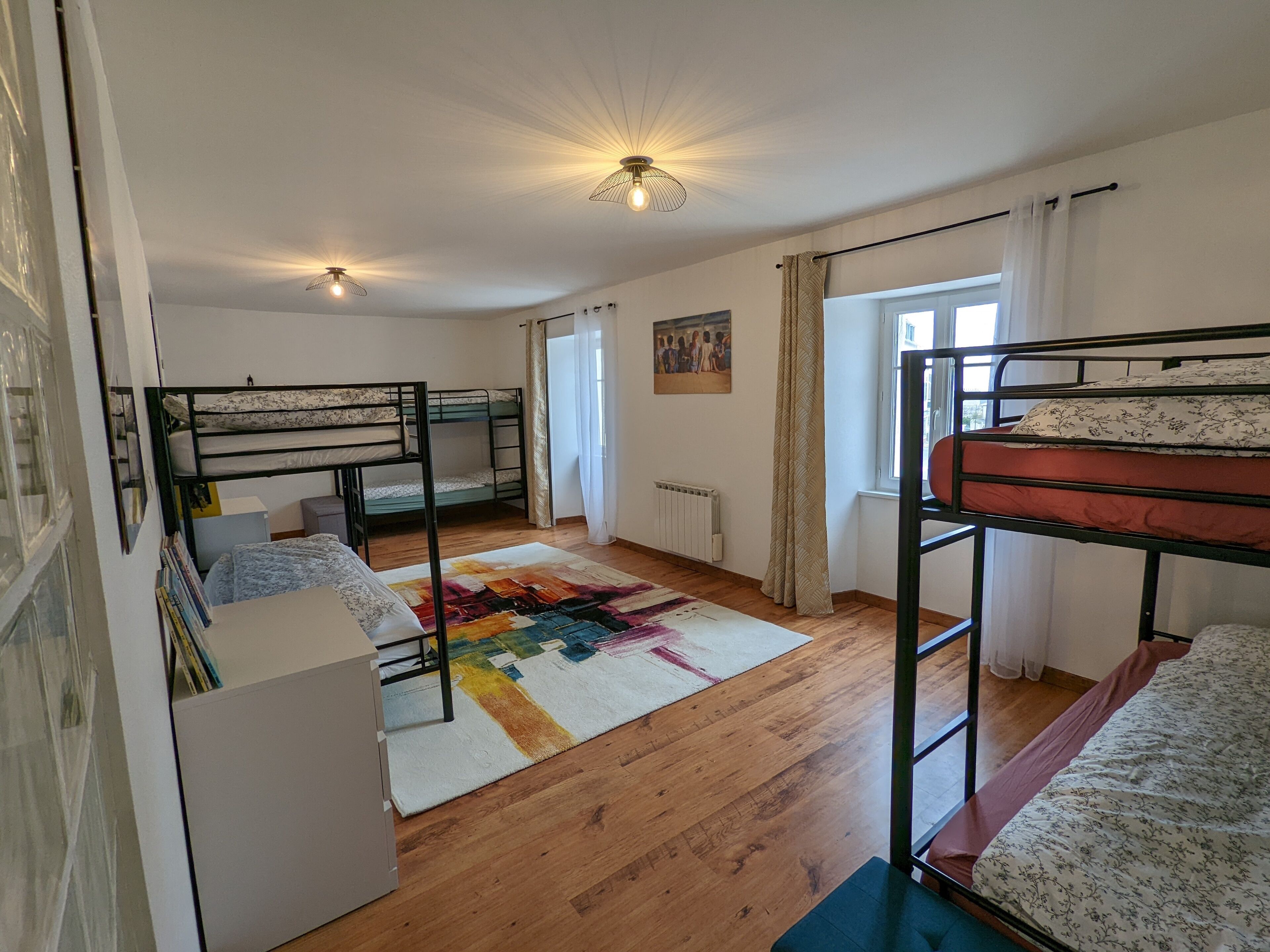 Ein Schlafsaalzimmer mit Etagenbetten, einem Heizkörper, einem bunten Teppich und einem Fenster mit Vorhängen.