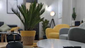 Ein modernes Wohnzimmer mit einem runden Tisch, einer Topfpflanze und einem schwarzen Wasserkocher.