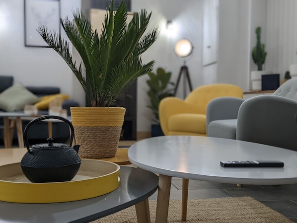 A modern living room with a round table, a potted plant, and a black kettle.