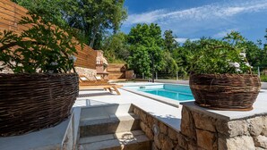 Une piscine avec des marches en pierre menant à l’eau, entourée d’une végétation luxuriante et d’une clôture en bois.