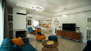 A spacious living room with a fireplace, a dining area, and a kitchen in the background.