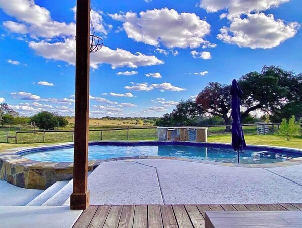 Relax by the pool surrounded by lush trees and a stone wall.