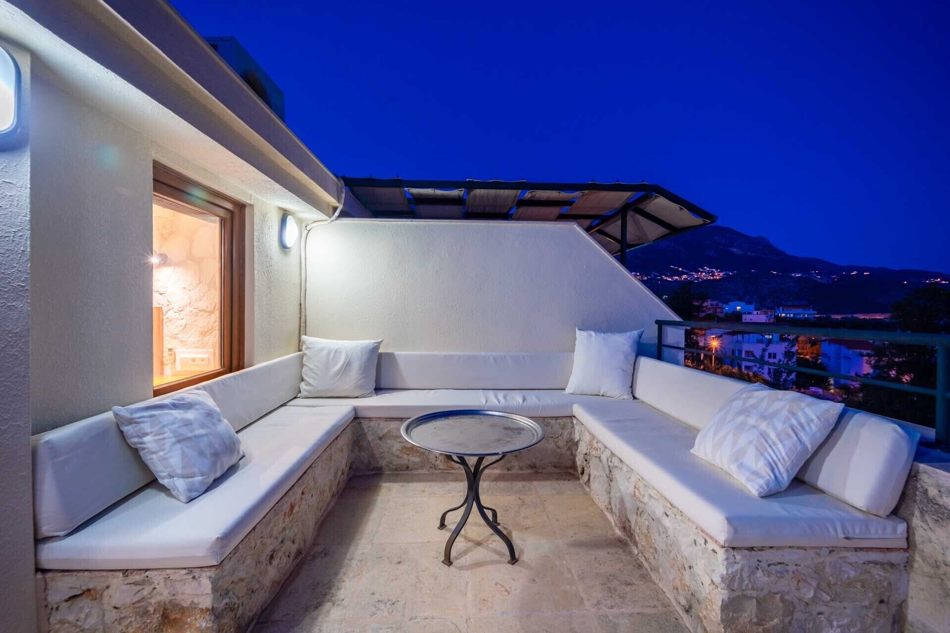 A cozy outdoor seating area with a stone wall, cushioned benches, and a small round table.