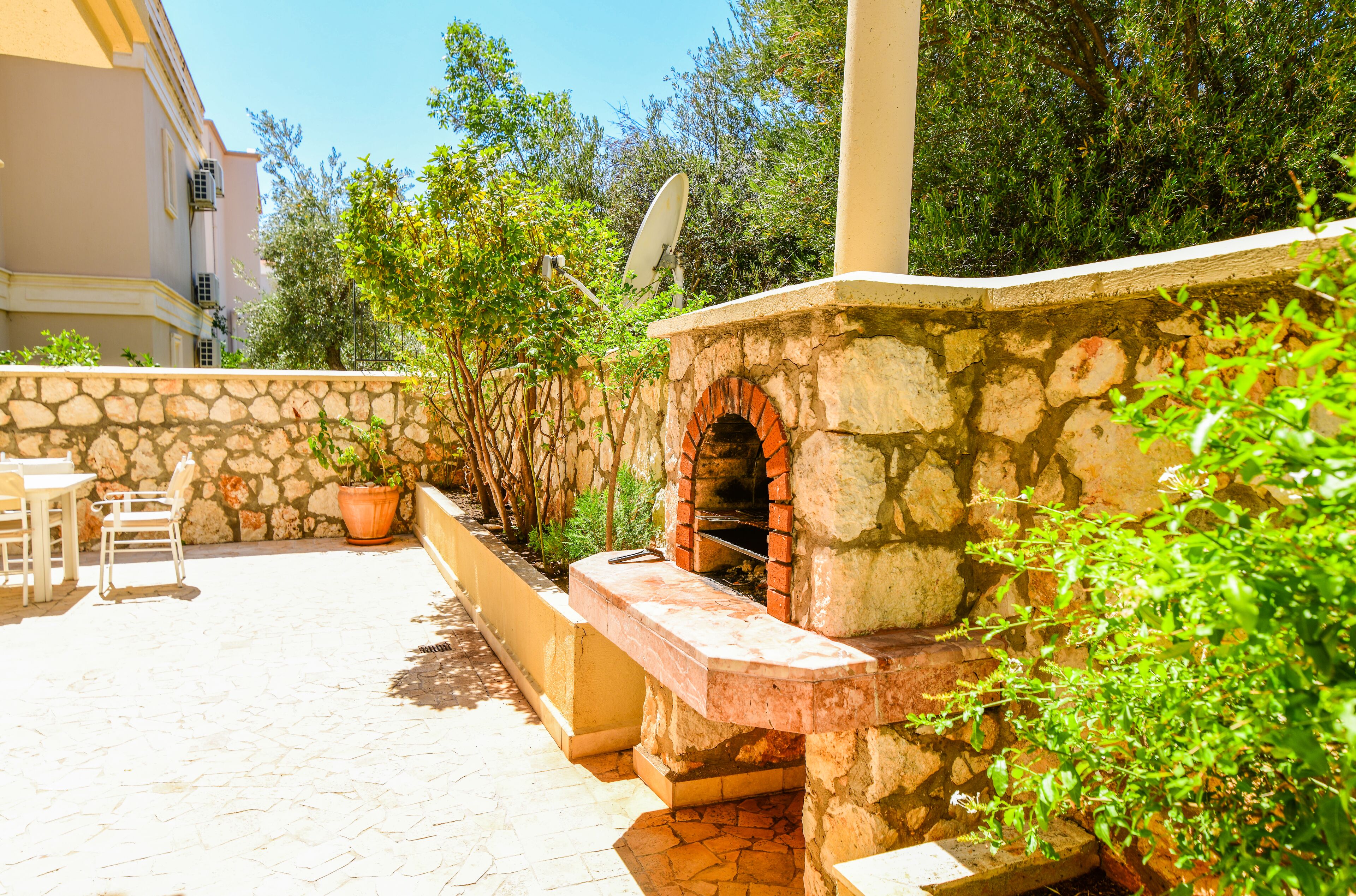 A stone-built outdoor kitchen area with a brick oven, surrounded by potted plants and a stone wall.