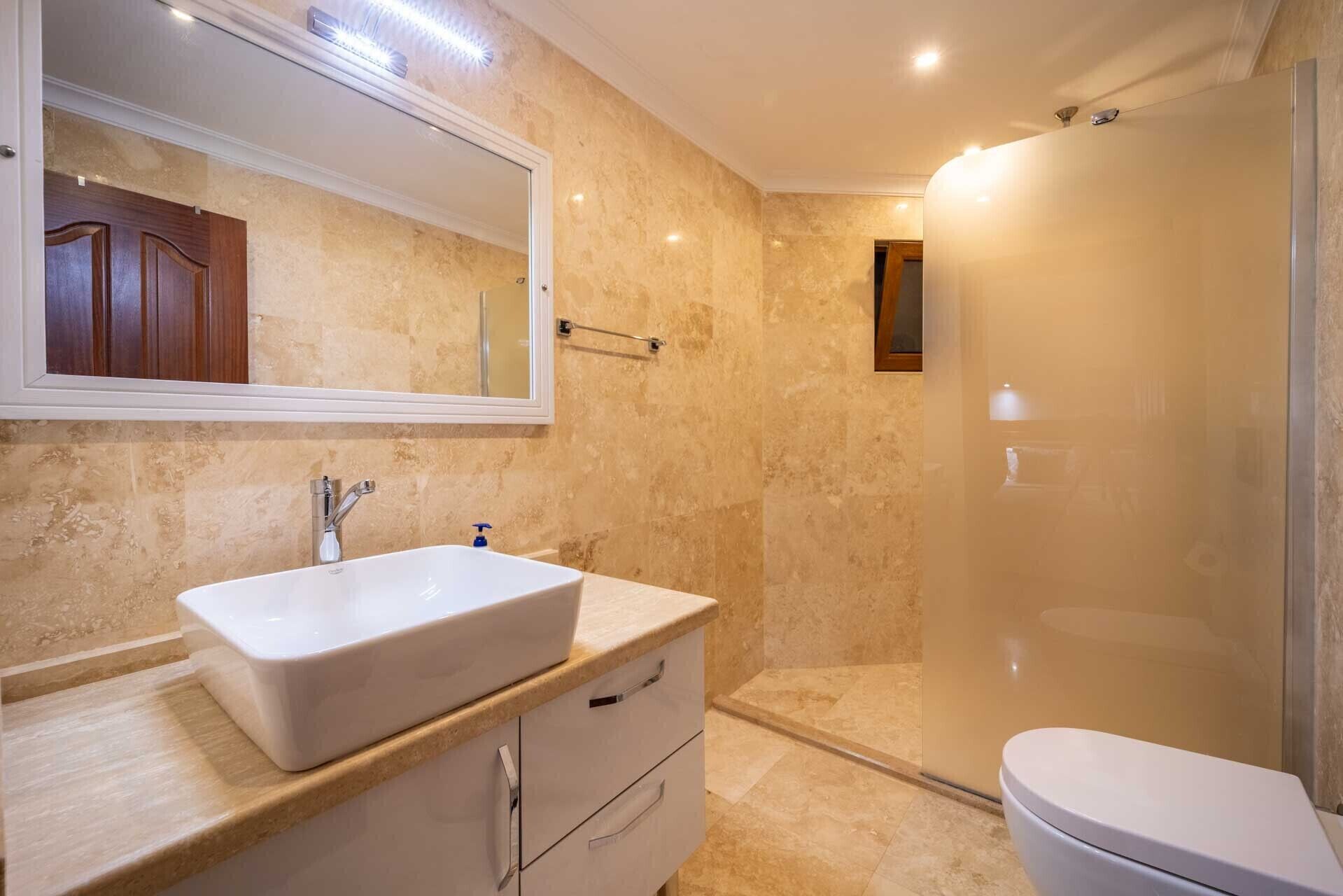 A bathroom with a large mirror, a sink, a toilet, and a shower.