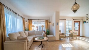 Un salon spacieux avec un canapé beige, une petite table ronde et un coin repas doté de chaises en osier.