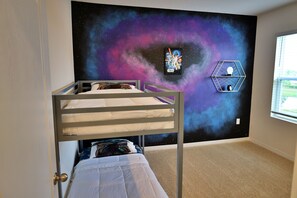 Quarto de criança com beliche, papel de parede com tema espacial e pôster de Star Wars.