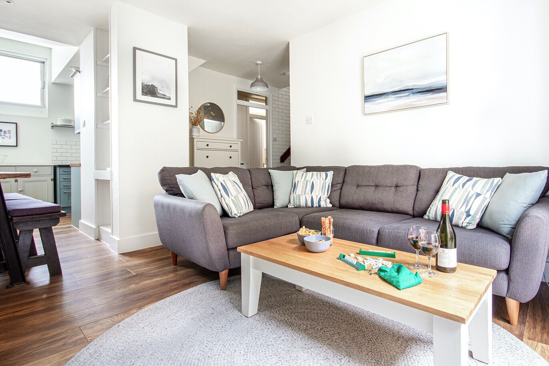 A modern living room with a grey sectional sofa, a wooden coffee table, and a kitchen in the background.