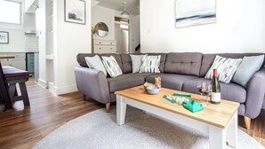 A modern living room with a grey sectional sofa, a wooden coffee table, and a kitchen in the background.