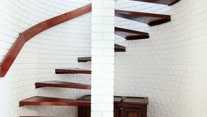 A spiral staircase with wooden steps and beams against a white brick wall, leading to a dark wooden cabinet.