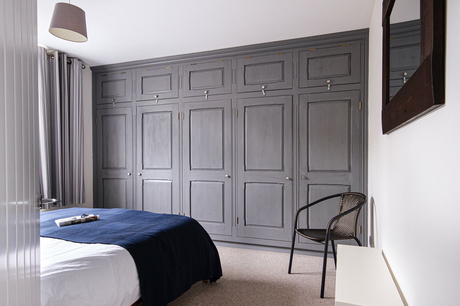 Quarto com cama, cadeira, guarda-roupa e espelho.