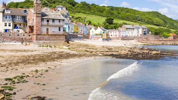 A coastal town with a prominent clock tower, colorful buildings, and a sandy beach.