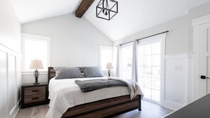 Une chambre à coucher avec un lit en bois, deux tables de chevet avec des lampes, une grande fenêtre avec des rideaux et un puits de lumière.