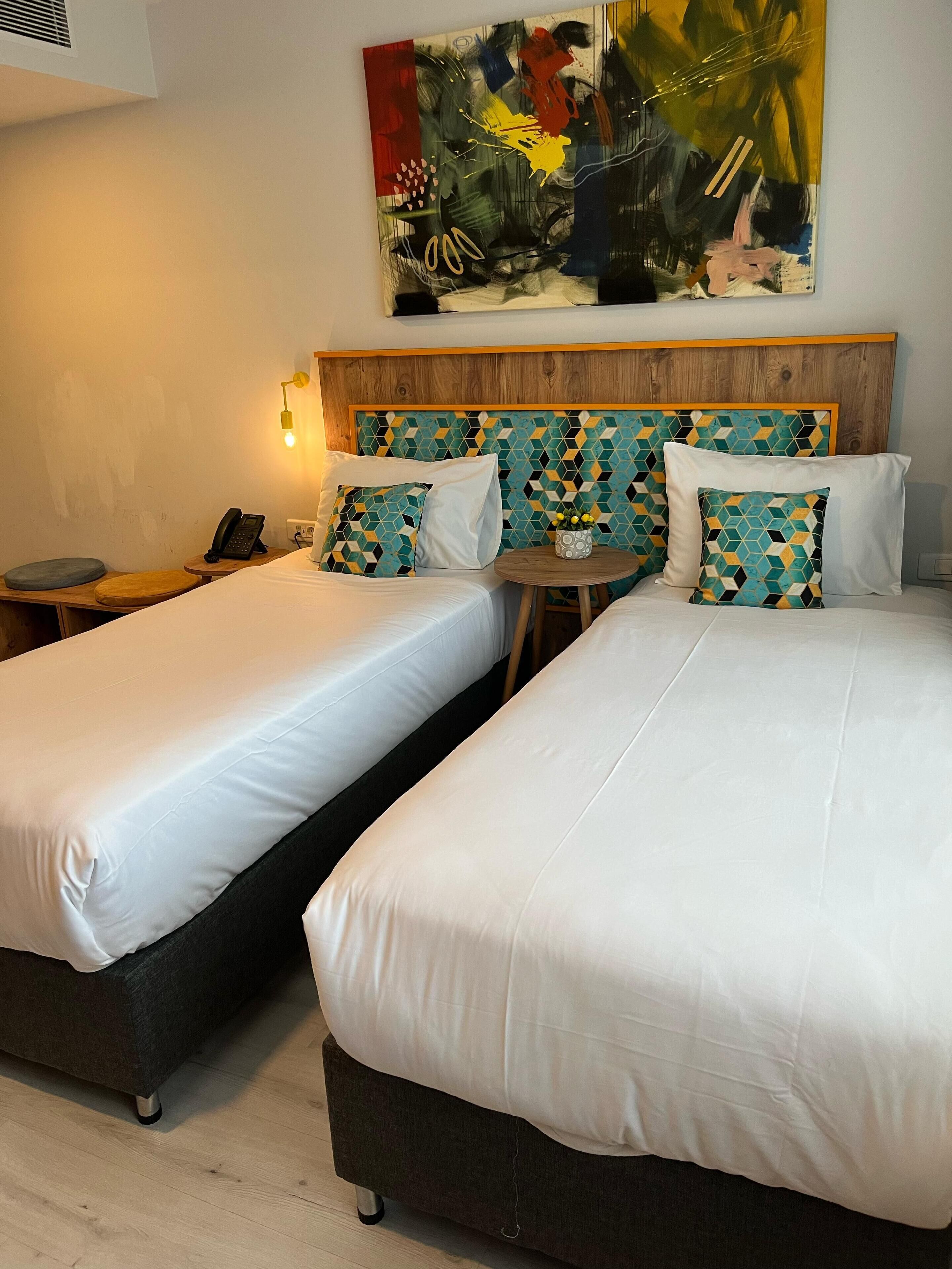 A hotel room with two beds, a wooden headboard, a small round table, and a wall-mounted phone.