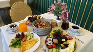 A breakfast setting with plates of food, including eggs, cheese, and vegetables, and a small vase with pink flowers. - The Gate Hotels Kadıköy Downtown (Istanbul)