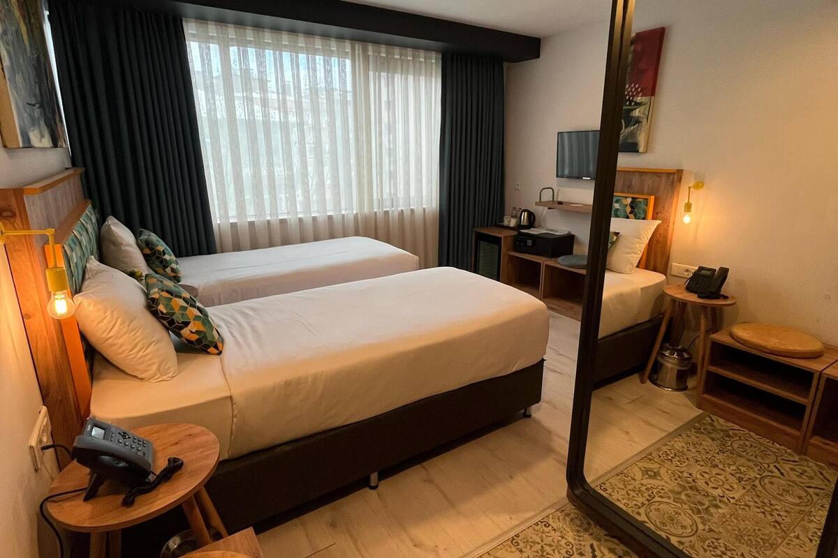 Una habitación de hotel con dos camas, un escritorio, una silla, un espejo y una pequeña mesa con lámpara.