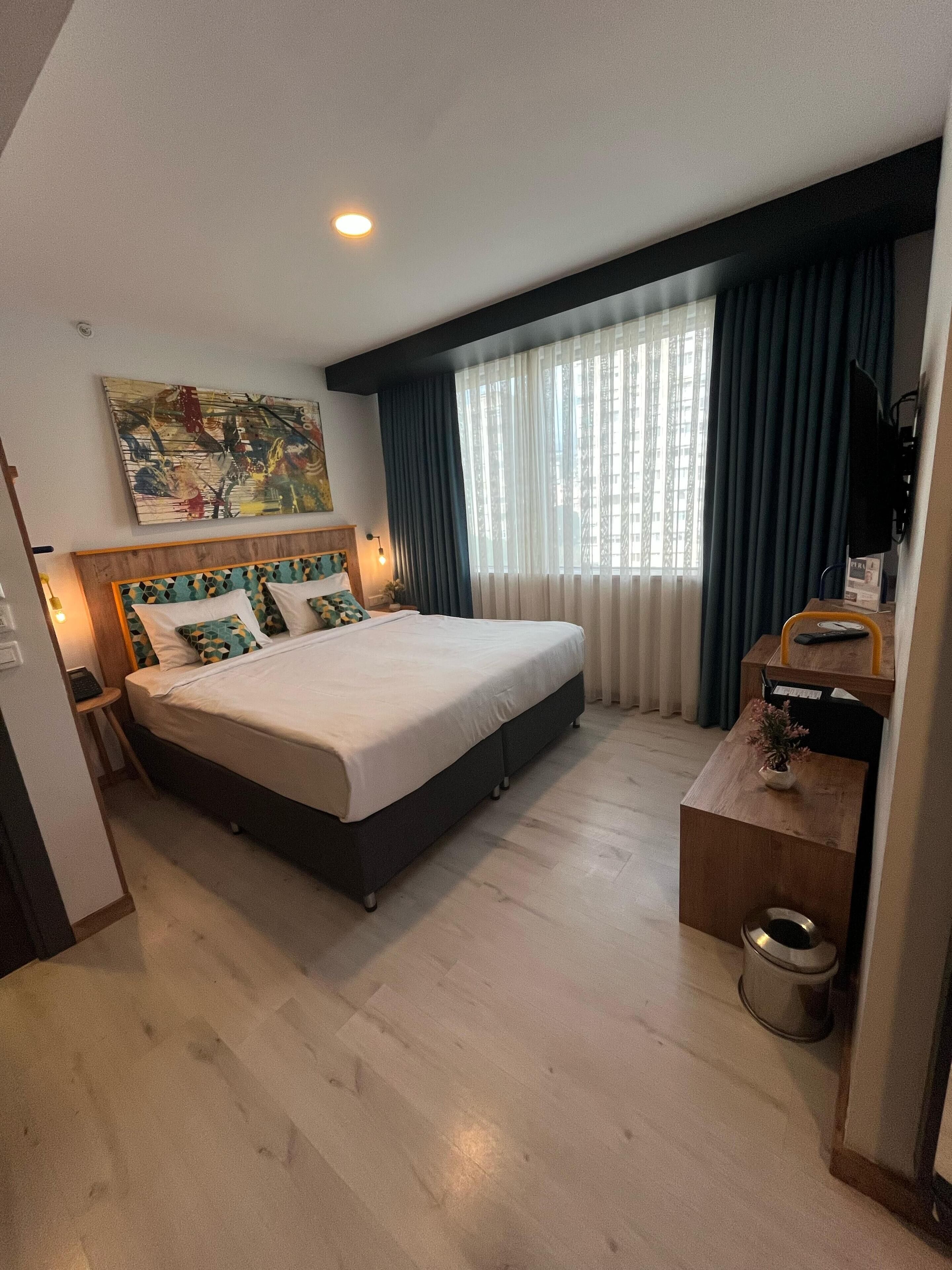 Ein Hotelzimmer mit Bett, Schreibtisch, Fernseher, einem Gemälde und einem Fenster mit Vorhängen.