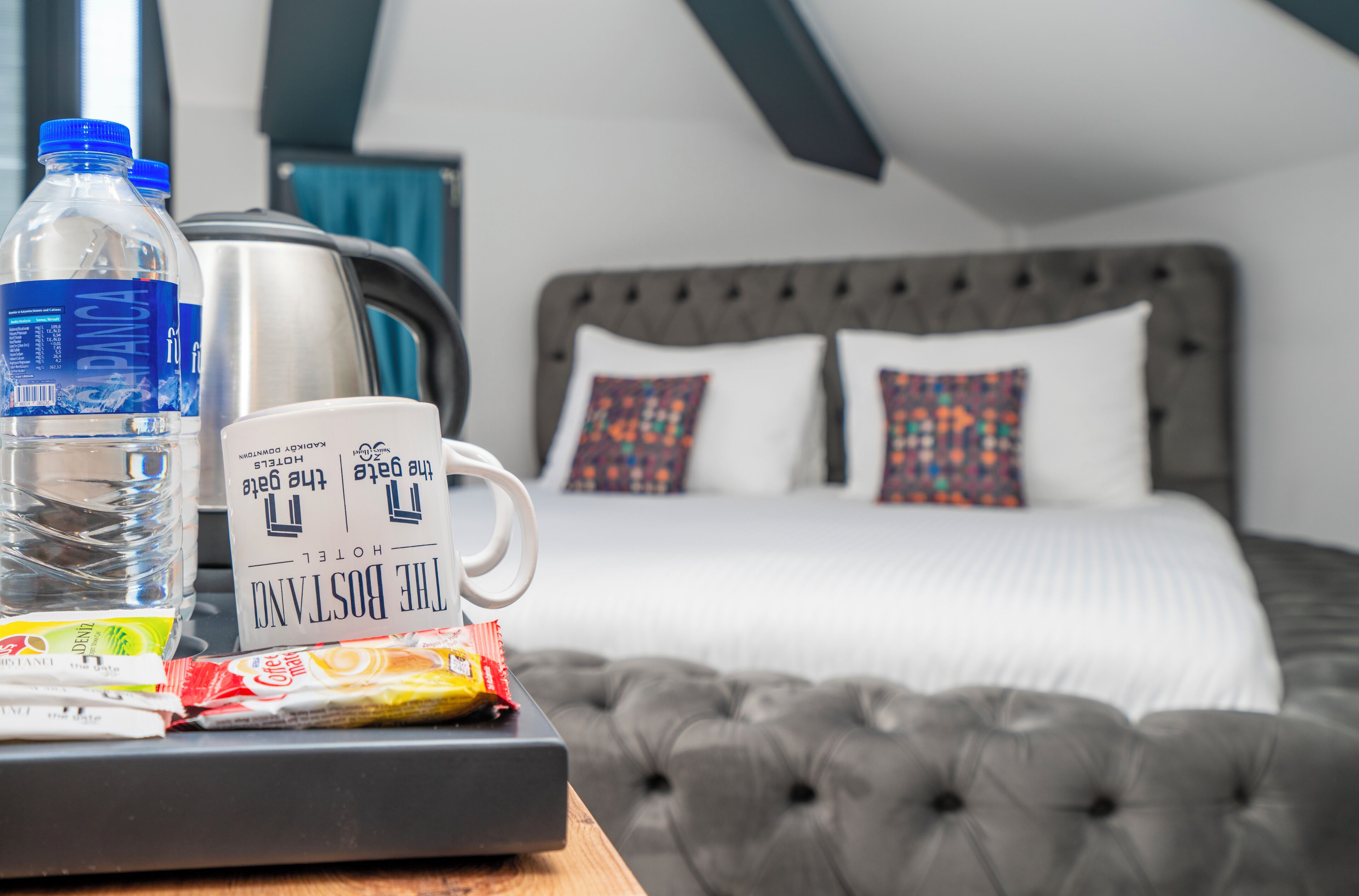 Habitación de hotel con cama, cafetera, botella de agua y un paquete de aperitivos sobre la mesita de noche.
