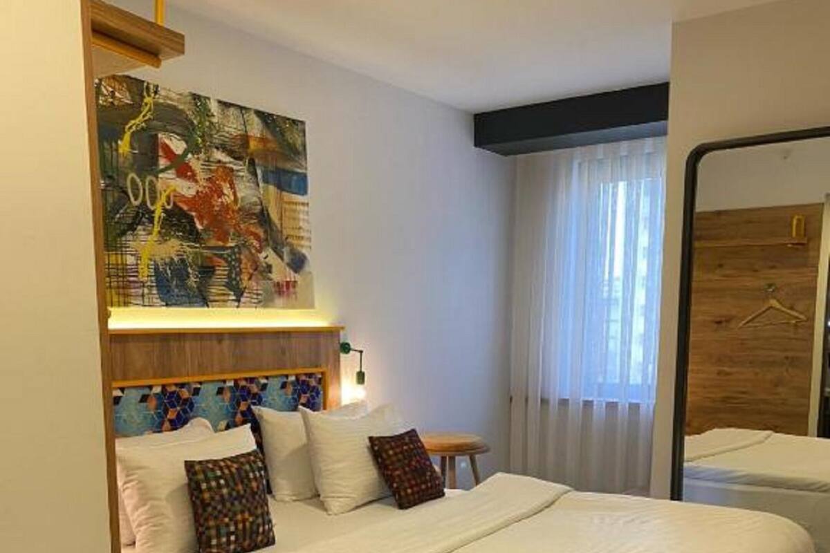 Una habitación de hotel moderna con una cama grande, una mesita, un cuadro y un armario de madera.