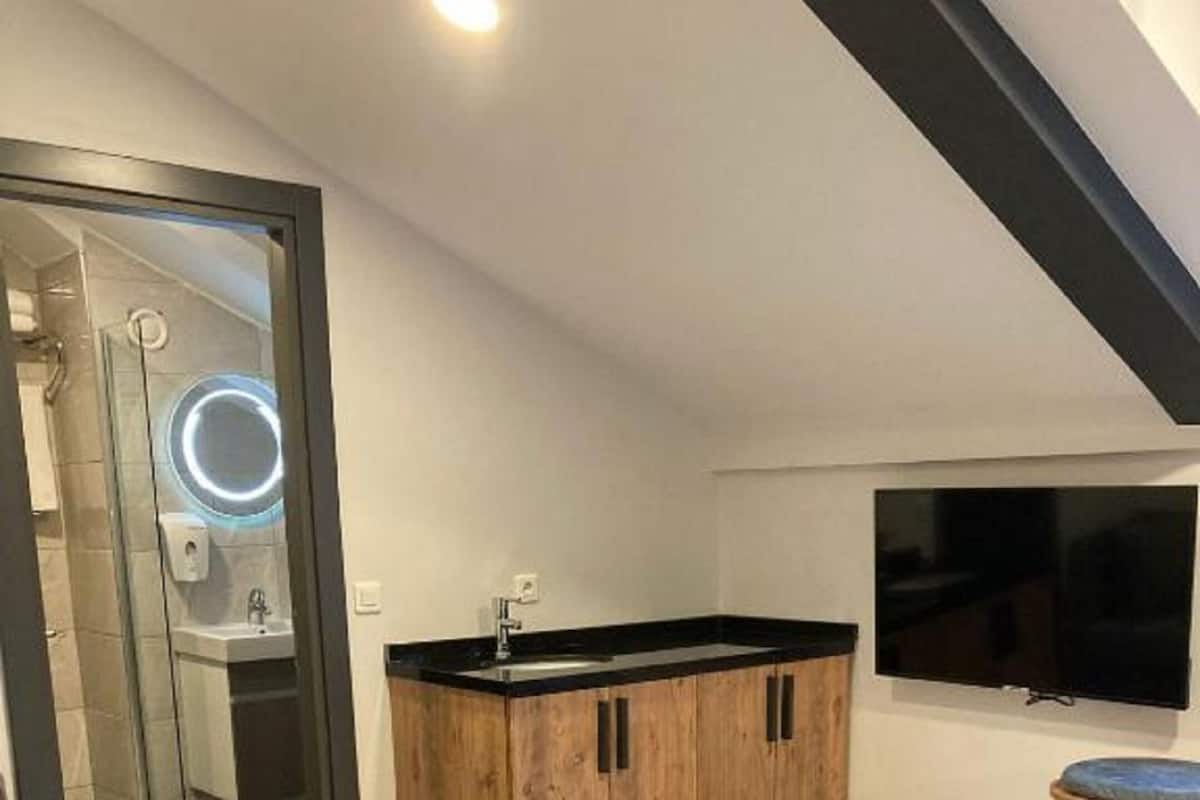 Un espacio habitable compacto con kitchenette, un televisor montado en la pared y una zona de estar con sofá y una mesita.