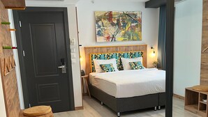 A modern hotel room with a bed, a chair, a small table with a plant, a door, and a painting on the wall. - The Gate Hotels Kadıköy Downtown (Istanbul)