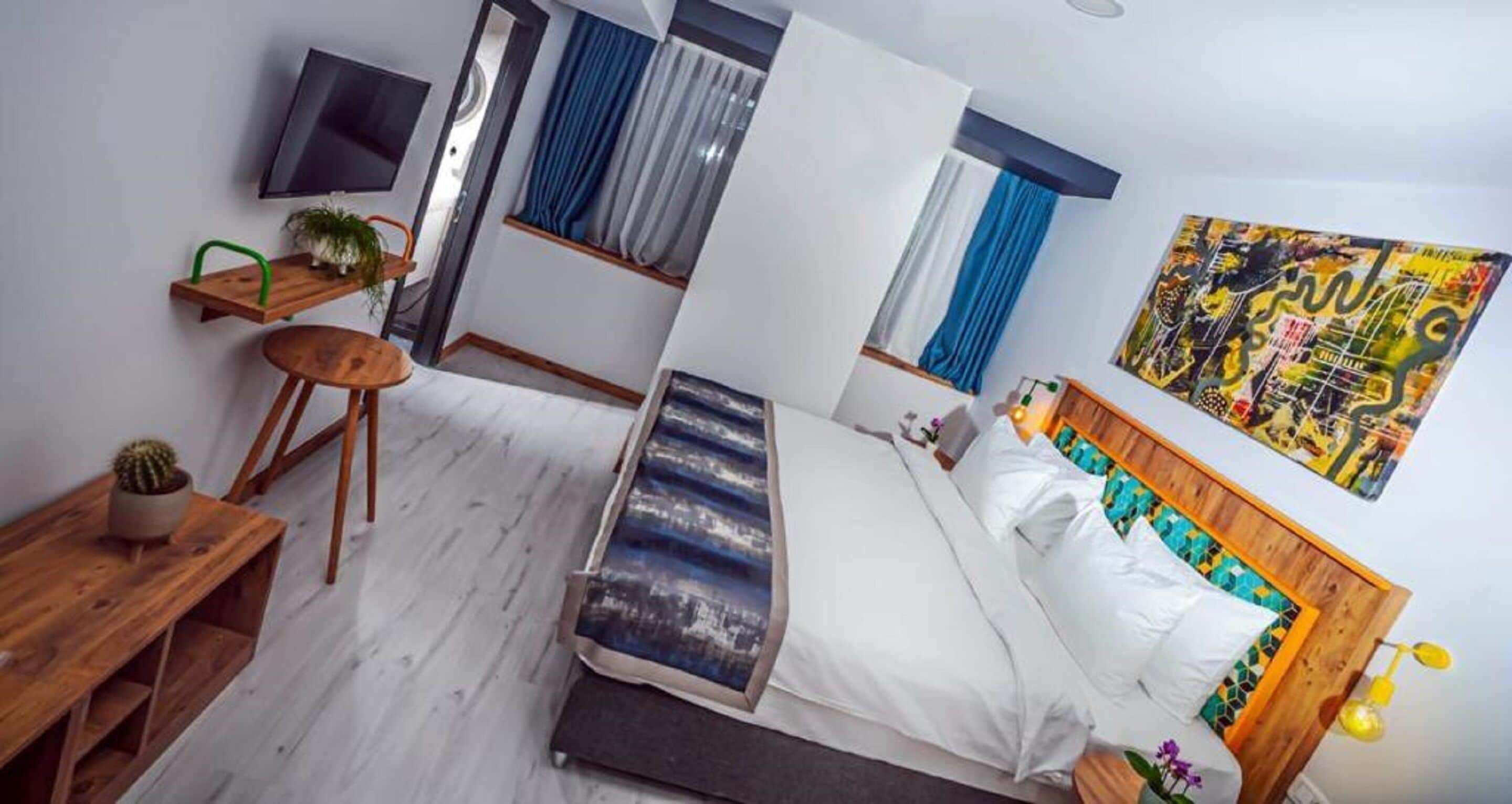 A modern hotel room with a bed, a desk, a chair, a TV, and a window with curtains.