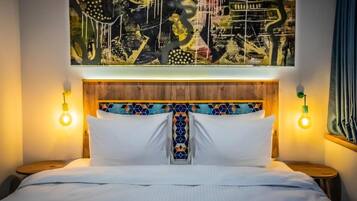 A hotel room with a bed, a headboard with a geometric pattern, and a large abstract painting above the bed.