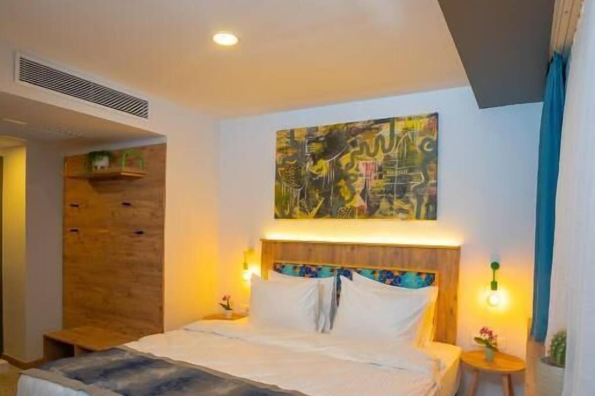 Un dormitorio moderno con una cama grande, un cabecero de madera, un cuadro abstracto colgado en la pared y una mesita de noche con una lámpara.