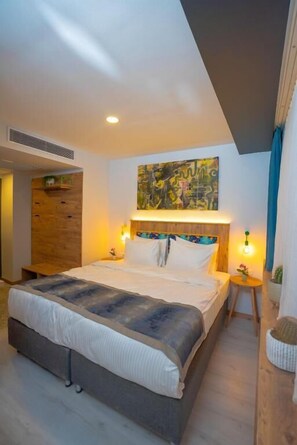 Ein modernes Schlafzimmer mit einem großen Bett, einem Holzkopfbrett, einem Wandbild im abstrakten Stil und einem kleinen Nachttisch mit Lampe.