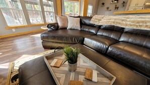 Un salon moderne doté d’un grand canapé d’angle, d’une table basse en bois et offrant une vue sur l’extérieur grâce à de grandes fenêtres.