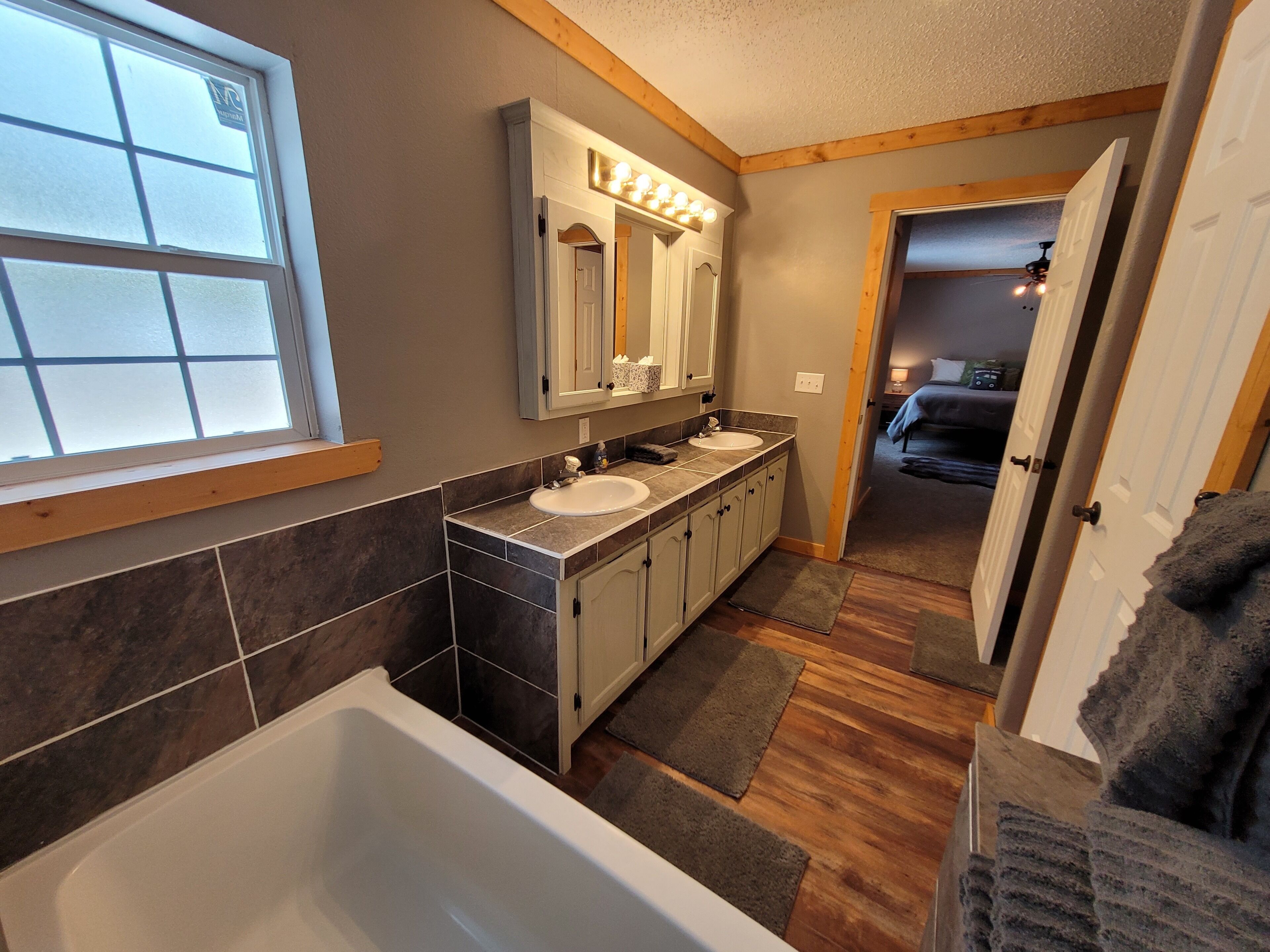 A bathroom with a bathtub, two sinks, a vanity, and a mirror with lights.