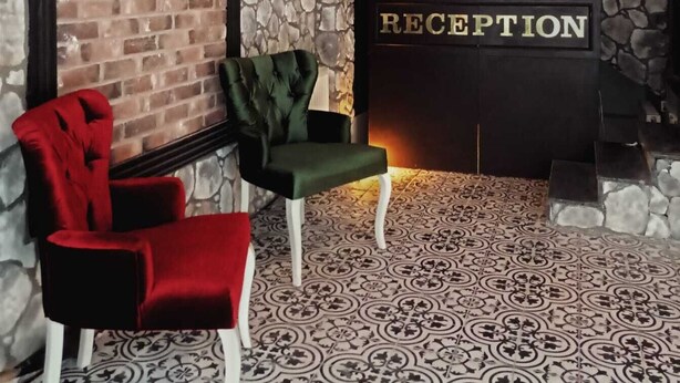 A reception area with a stone wall, a brick wall, and a reception sign. There are two chairs, one red and one green, and a patterned floor. - Begonvil Pansiyon Konaklama (Izmir)
