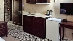 A kitchen with dark wooden cabinets, a white countertop, a built-in sink, a small refrigerator, a stove, and a microwave. - Begonvil Pansiyon Konaklama (Izmir)
