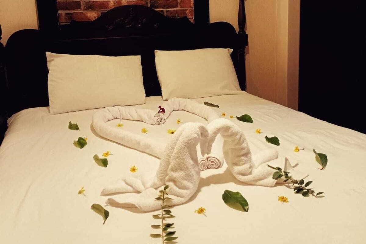 Ein ordentlich bezogenes Bett mit weißer Decke, zwei Kissen und einer dekorativen Handtuchanordnung mit Blumen und Grünpflanzen.