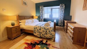 A hotel room with a bed, bedside tables, a desk, and a window with curtains. - Beautiful Rural 3BR Cottage with Stunning Views - Pass the Keys (Dumfries)