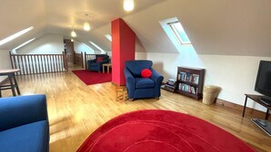 A spacious loft with a high ceiling, wooden flooring, a red accent wall, a blue armchair, a bookshelf, and a television. - Beautiful Rural 3BR Cottage with Stunning Views - Pass the Keys (Dumfries)