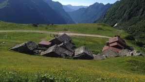 Uma aldeia montanhosa no campo, com casas de pedra tradicionais, estrada de terra e vegetação exuberante.