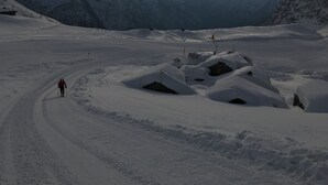 Paisagem montanhosa nevada com um caminho aberto até um abrigo.