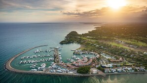 Une vue aérienne d’une marina où sont amarrés des bateaux, entourée de zones résidentielles et bordée par une vaste étendue d’eau.