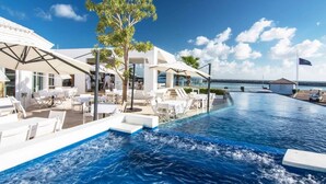 Un espace aménagé au bord de la piscine, avec des chaises longues et des parasols, une vue dégagée sur la mer et un drapeau.