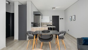 A modern kitchen with a central island, a dining area with a table and chairs, and a living area with a sofa. - Light and Cozy Blouberg Apartment (Cape Town)