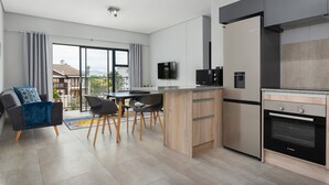 A modern kitchen with a built-in oven, a dining area with a table and chairs, and a large window offering a view of the outdoors. - Light and Cozy Blouberg Apartment (Cape Town)